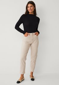 Schwarzes Langarmoberteil, beige High-Waist-Jeans und zweifarbige Ballerinas mit einer schwarzen Zehenkappe. Glatte Textur, figurbetontes Design und zulaufendes Bein.