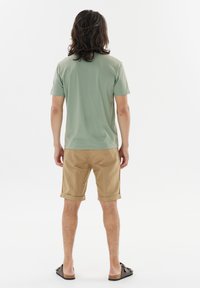 Light green short-sleeve tee paired with beige shorts, featuring rolled cuffs, smooth texture, and casual slip-on footwear.