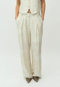 Lichtbeige, hoge taille broek van een gestructureerde stof, met voorplooien, zijzakken en brede benen, gecombineerd met puntige metallic schoenen.