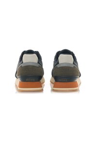 Zapatillas de hombre que presentan una mezcla de nobuk azul marino oscuro y verde oliva, con un talón de cuero blanco. La suela de goma es beige con un acento marrón.