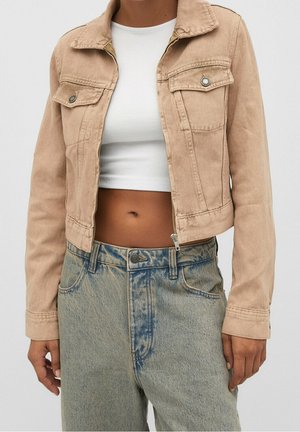 Person wearing a beige cropped denim jacket over a white cropped top and high-waisted light-washed blue jeans.