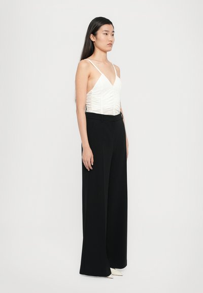 Haut blanc ajusté avec fronces, décolleté en V et fines bretelles, associé à un pantalon noir en large jambe taille haute et des chaussures blanches à bout pointu.