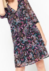 Svart klänning med v-ringning, trekvartslånga ärmar, lagerdesign, med ett färgglatt paisleymönster i rosa, blått och lila.