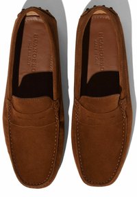 Braune Wildleder-Slipper mit gestickten Details, flachen Sohlen und einer glatten Textur. Das Branding ist auf der Innensohle eingeprägt. Keine auffälligen Beschläge oder Akzente.