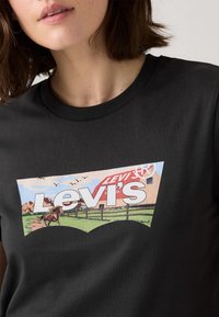 Svart bomull t-skjorte med et fargerikt grafisk design av en hest og et stabbur, med "Levi's"-tekst, rundt halsutskjæring og korte ermer.