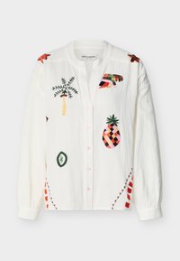 Chemise blanche boutonnée avec des motifs tropicaux colorés brodés comprenant un ananas, un palmier et des formes abstraites à l'avant et sur les épaules.