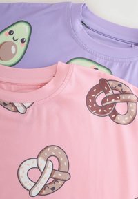 Due t-shirt: una lavanda con una grafica di avocado e una rosa con due pretzel. Tessuto morbido con colori vivaci e design in stile cartone animato.