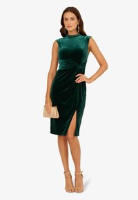 Zielona sukienka z aksamitnego materiału z wysokim kołnierzem, krótkimi rękawkami, skręconym detalem w talii oraz rozcięciem do uda, w połączeniu ze złotą kopertówką.