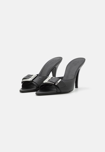 Black open-toe mules with a high heel, made of smooth leather. Features a large silver buckle accent and pointed toe design.
