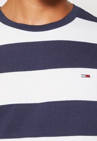 Camiseta de algodón con rayas horizontales en azul marino y blanco. Cuenta con un cuello redondo y un pequeño logo en rojo, blanco y azul en el pecho.