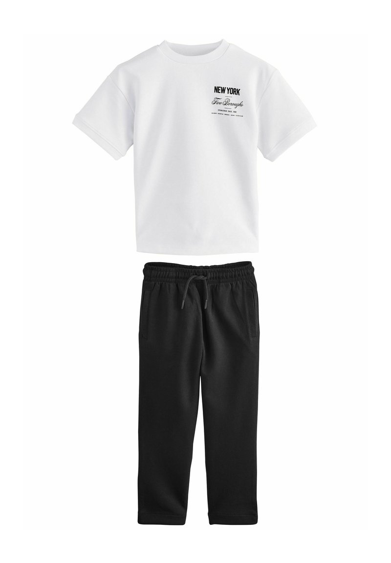 Hvid t-shirt med korte ærmer og sort tekst, parret med sorte sweatpants med elastisk talje og sidelommer.