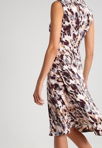 Ärmlös klänning i ett flerfärgat abstrakt mönster med bruna, grå och persikofärgade nyanser, med en figurnära bodice och ett flödande kjol.