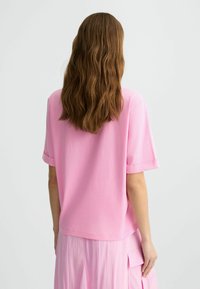 Top rosa a maniche corte con vestibilità rilassata, caratterizzato da maniche arrotolate e orlo posteriore leggermente più lungo; realizzato in tessuto leggero e morbido.