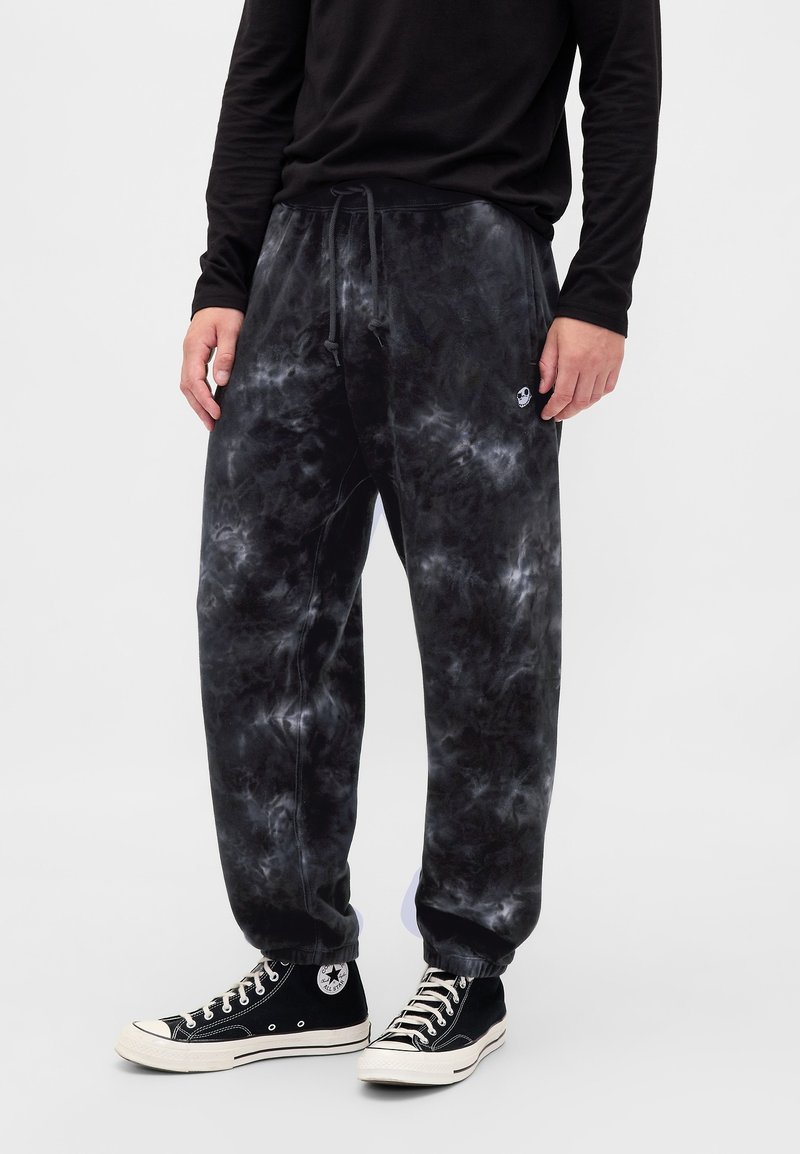 Czarne spodnie dresowe z efektem tie-dye posiadają elastyczną talię ze sznurkiem, boczne kieszenie oraz mały akcent w postaci logo. Połączone z czarnymi sneakersami.