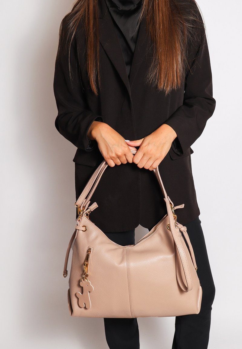 Beige leren hobo tas met een gestructureerde afwerking, gouden hardware en een decoratieve charm. Beschikt over dubbele schouderbanden en een ritsvak.