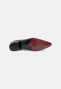 Suela de zapato de cuero negro con forma puntiaguda. Presenta un patrón embossado, tachuelas de acento dorado y un tacón burdeos con detalles grabados.