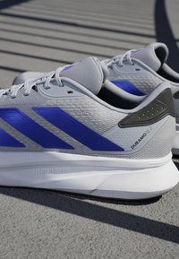 Gray athletic shoes with blue stripes, textured upper, padded collar, and white sole. Features "LIGHTMOTION" branding on the side.