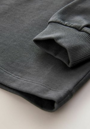 Grauer Pullover mit gerippten Bündchen, weichem Gefühl und sauberer Naht, mit einem Stoff, der über einer Fläche hängt.
