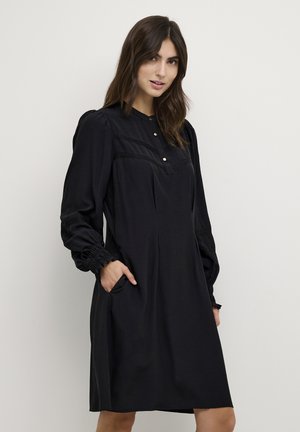 Black dress with long puff sleeves, button placket, subtle pleating, and smocked cuffs. Features side pockets. Smooth fabric texture.