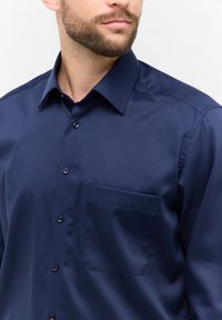 Navyblauw overhemd met knoopsluiting van soepel stof, met een puntige kraag en een enkele borstzak. Subtiele glans en op maat gemaakte pasvorm.