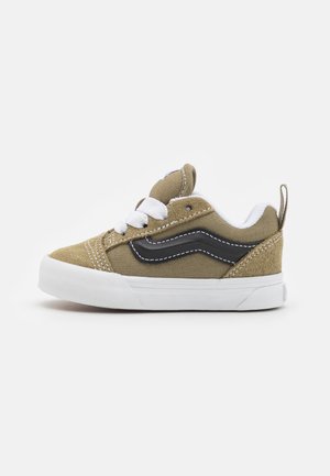 Zapatillas de lona verdes con cordones blancos, raya lateral negra y suela de goma blanca. Presenta detalles de costura y un tirador en el talón. Diseño duradero.