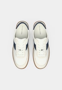 Baskets blanches avec un panneau d'accent bleu marine, une tige en cuir lisse, des côtés en tissu texturé, et une semelle en caoutchouc couleur gomme avec fermeture à lacets.