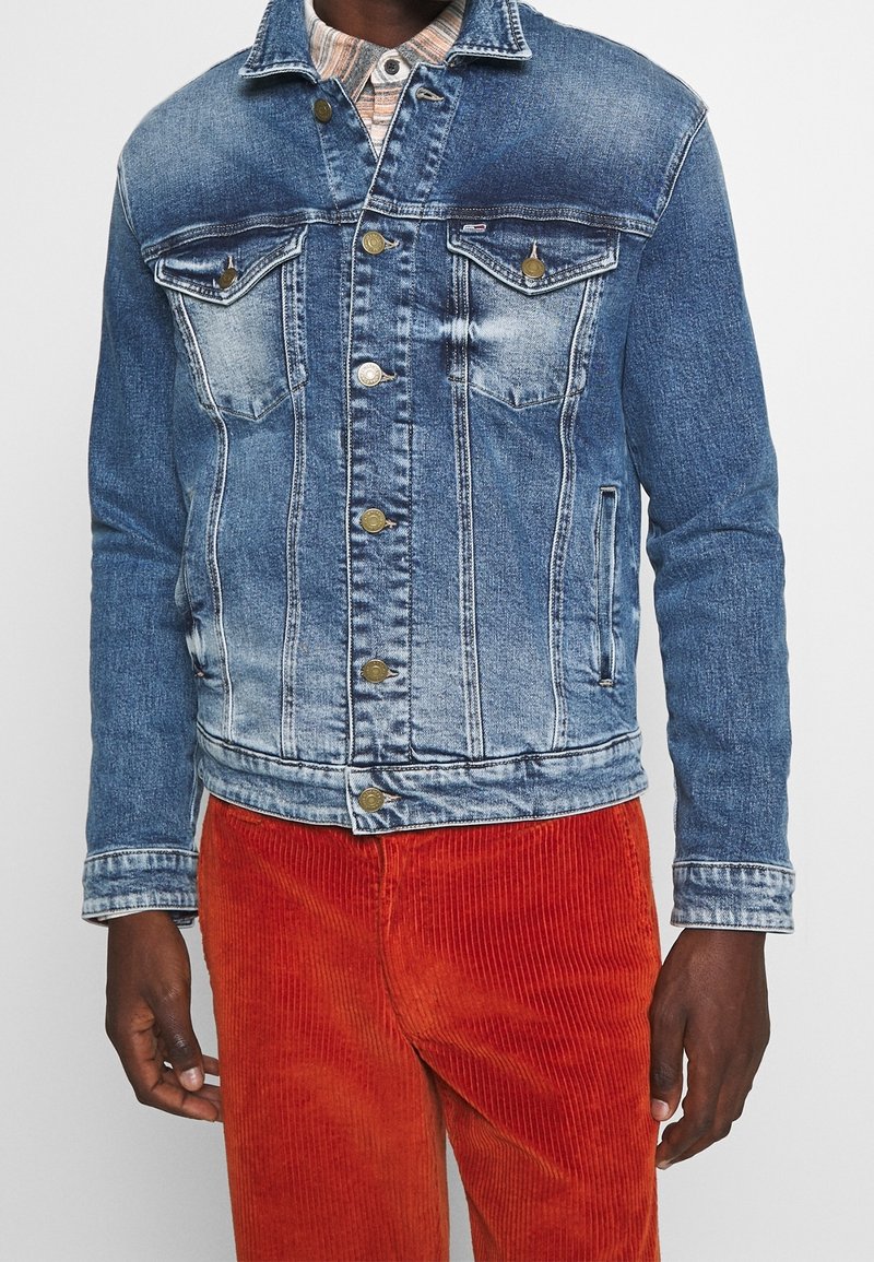 Džínová bunda v světle modré barvě s vybledlými místy, má dvě náprsní kapsy a zlaté knoflíky. Nošena s oranžovými manšestrovými kalhotami.