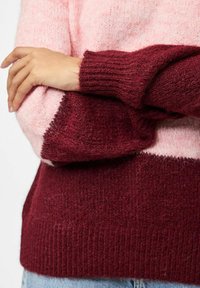 Pleteni pulover s dizajnom u blokovima boja, s mekanom ružičastom gornjom sekcijom i tamnocrvenom donjom sekcijom, rebrastim rukavima i teksturom.