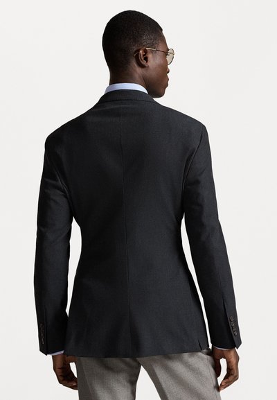 Ραμμένο μαύρο σακάκι με λεία υφή, δομημένους ώμους και μονό ανοίγμα. Διαθέτει τέσσερα κουμπιά σε κάθε μανσέτα και μια ανοιχτό μπλε επένδυση στον γιακά.