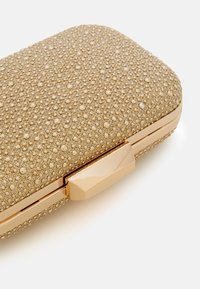 Pochette ton or avec une surface texturée ornée de petites perles, forme rectangulaire, et une fermeture à clapet métallique. Des accents métalliques lisses rehaussent le design.