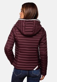 Giacca imbottita bordeaux con cappuccio, caratterizzata da un design trapuntato, chiusura con zip e tessuto testurizzato. Abbinata a jeans blu.