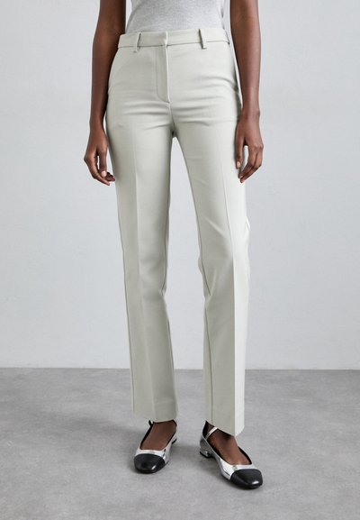 Pantaloni eleganți gri deschis, confecționați dintr-un material neted, cu un design drept și buzunare frontale. Asortați cu balerini argintii și negri.