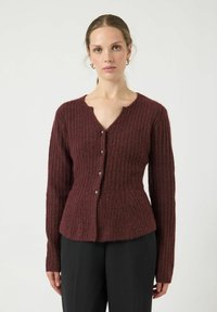 Cardigan ribbed color bordeaux con scollo a V, maniche lunghe e cinque bottoni decorativi sul davanti. Texture morbida, design attillato.