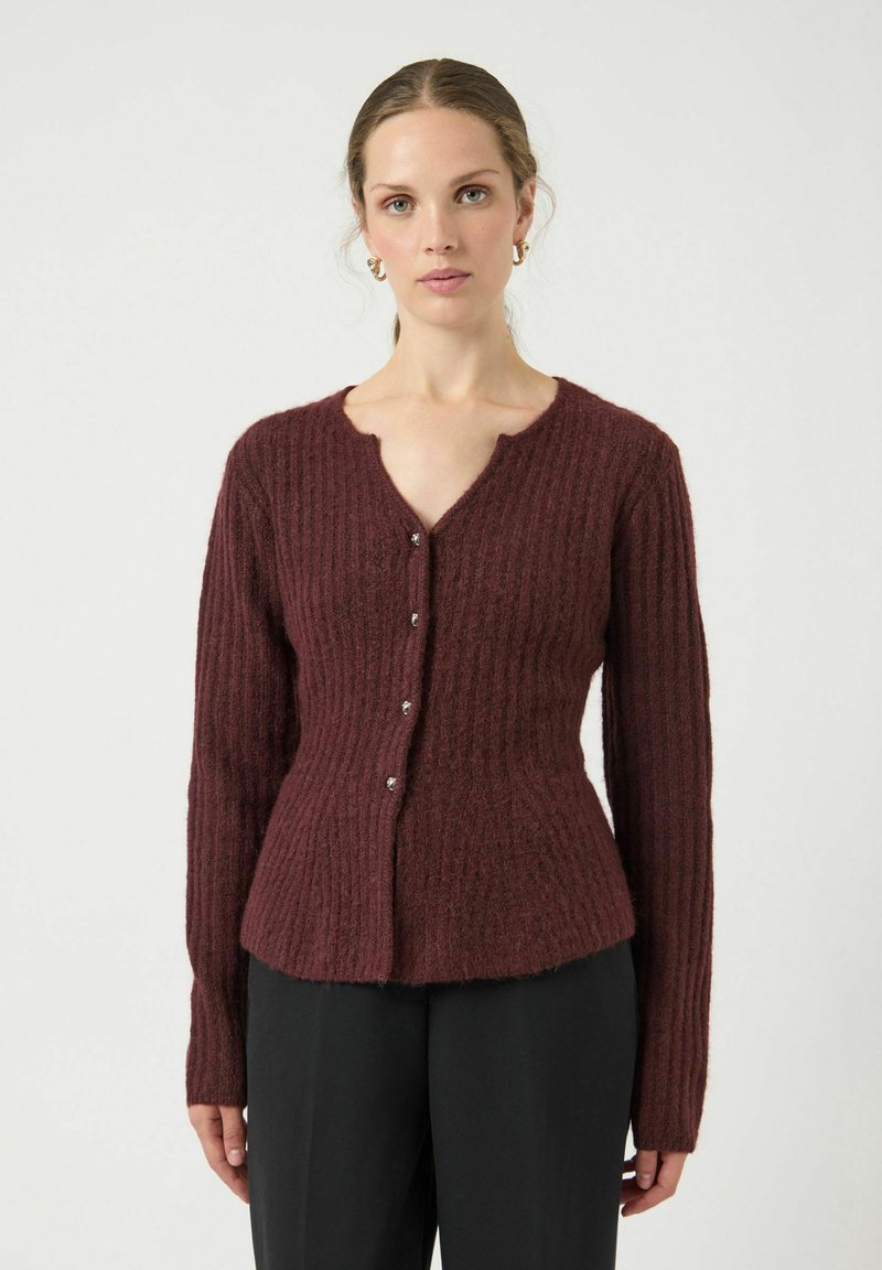 Cardigan ribbed color bordeaux con scollo a V, maniche lunghe e cinque bottoni decorativi sul davanti. Texture morbida, design attillato.