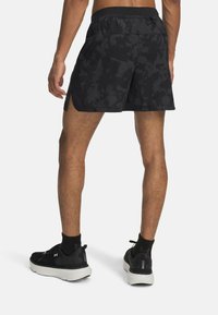 Svarta träningsshorts med ett kamouflage-mönster, sidoflikar och andningsbart tyg. Bärs med svarta löparskor med vita sulor.