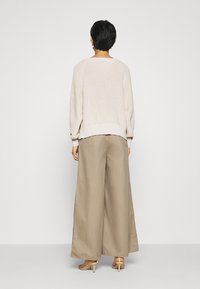 Pull en maille beige clair à manches longues, assorti d'un pantalon large marron clair. Texture lisse et coupe décontractée.