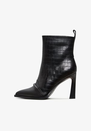 Czarne botki za kostkę z teksturą krokodyla, szpiczaste noski, gładkie wykończenie ze skóry i wysoki obcas w szpilce. Posiadają pętlę do łatwego zakładania.