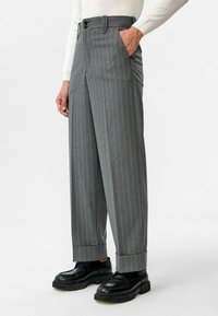 Grijs gestreepte broek met een hoge taille, wijde pijpen, twee zijzakken en zwarte knoopdetails, gecombineerd met zwarte schoenen.