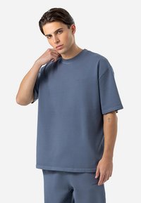 Per didelė mėlyna medvilninė marškinė su apvalia iškirpte ir trumpomis rankovėmis. Savybės: subtilus prekės ženklas ant krūtinės ir lygus paviršius.