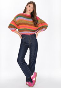 Maglione lavorato a maglia colorato con strisce multicolori, maniche a palloncino oversize; jeans in denim scuro; sneakers rosa e bianche con superficie testurizzata.