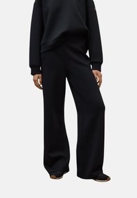 Pantalones de chándal anchos y negros, confeccionados con una tela suave que cuenta con una cintura elástica y un diseño minimalista. Adecuados para un estilo casual y para máxima comodidad.