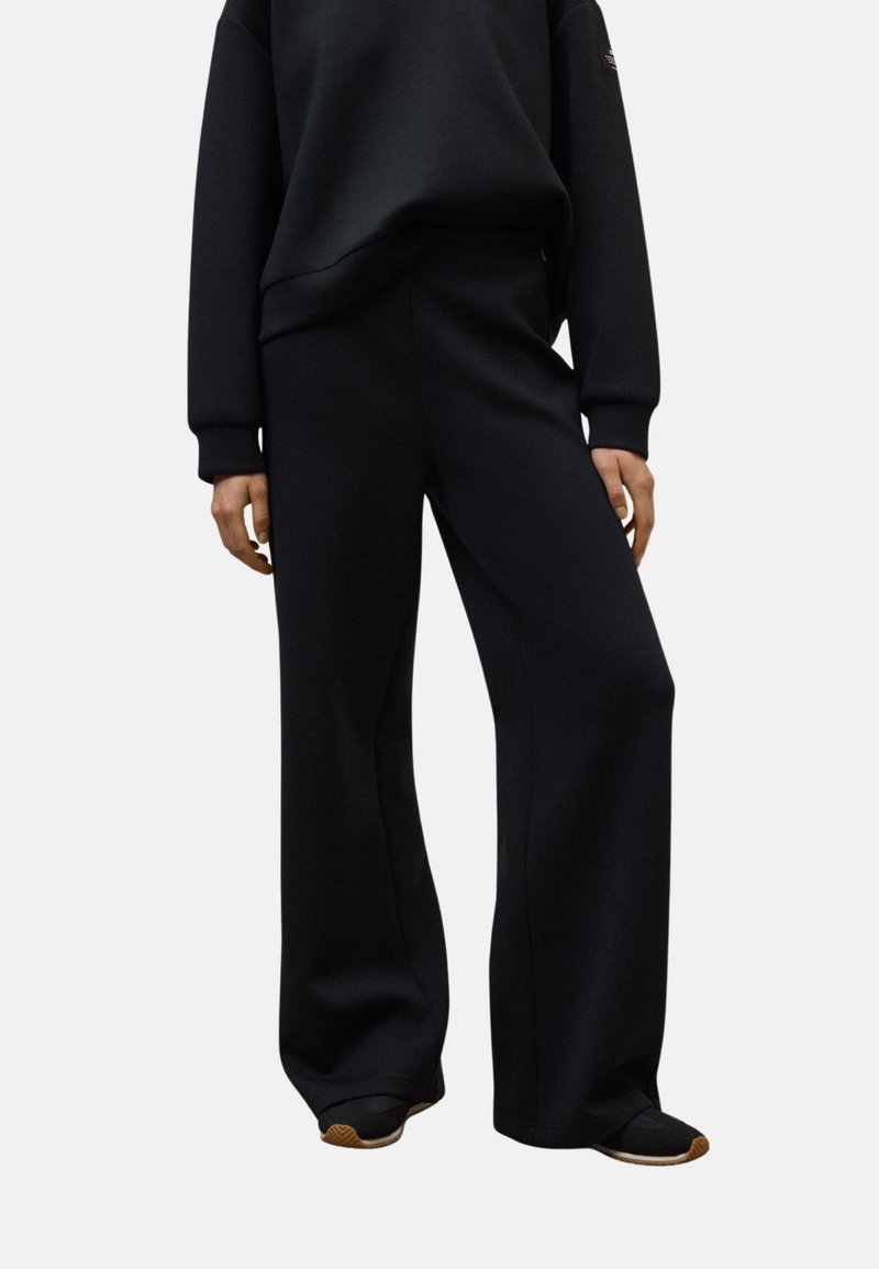 Pantalones de chándal anchos y negros, confeccionados con una tela suave que cuenta con una cintura elástica y un diseño minimalista. Adecuados para un estilo casual y para máxima comodidad.