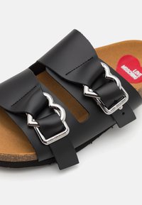 Sandal negru cu talpă slide, având două curele late, catarame metalice în formă de inimă și o talpă din plută cu parte inferioară de culoare bej.