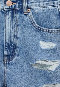 Gros plan sur la poche d'un jean en denim bleu clair avec des rivets en cuivre et des déchirures effilochées sur le tissu sous la poche.