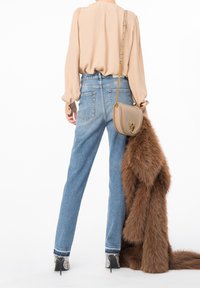 Beige paita, korkeavyötäröiset vaaleansiniset farkut, beige käsilaukku kultaisilla yksityiskohdilla ja ruskea tekoturkisviitta kädessä. Mustat kuvioidut korkokengät.