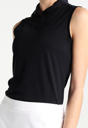 Femme portant une chemise noire sans manches à col rentrée dans un pantalon blanc taille haute, vue du cou aux hanches.