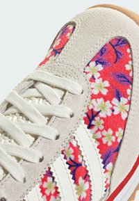 Sneaker med övre i vit mocka, livfullt blommönster i rött, rosa och blått. Har vita randiga detaljer och texturerade snören.