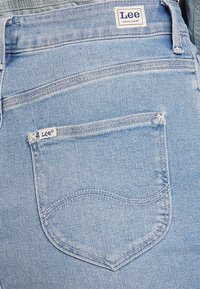 Ljust blå denimjeans med en bakficka som har en böjd design. Inkluderar en vit etikett med "Lee" och detaljer i sömmen.