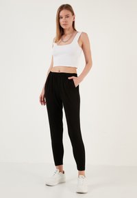 Zwarte joggingsbroek met elastische tailleband en zijzakken, gecombineerd met een witte geribbelde crop top en witte sneakers.