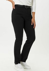 Pantaloni neri su misura con un design aderente, caratterizzati da un giro vita medio e una texture di tessuto liscia, abbinati a una cintura nera e sneakers bianche.